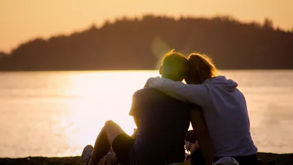 Image d'un couple enlacé au bord de l'eau au coucher du soleil